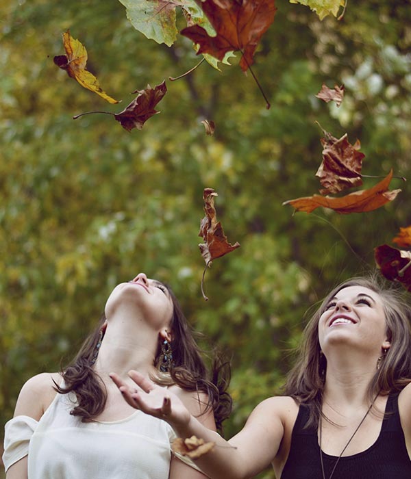 dos chicas jóvenes observan unas hojas de otoño que han lanzado al aire